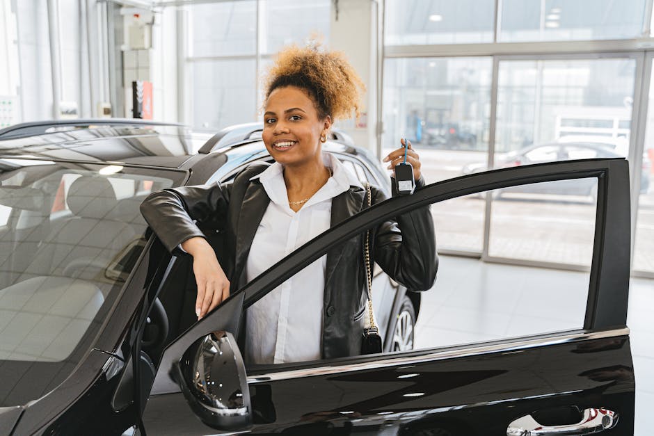 Smiling woman holding car key in dealership showroom next to new vehicle.